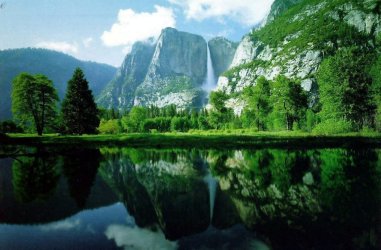 Fotografa de un bello paisaje. Se ven unas montaas al fondo y en primer plano un ro rodeado de rboles y hierba muy verde.