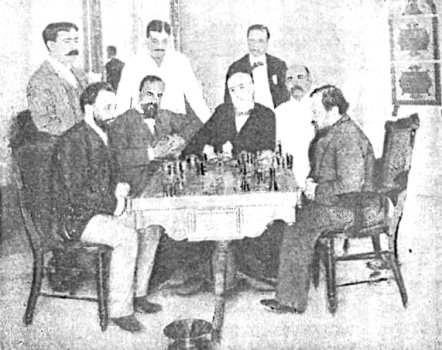 Chigorin y Steinitz ante el tablero, rodeados de 3 personas sentadass y otras 3 de pie